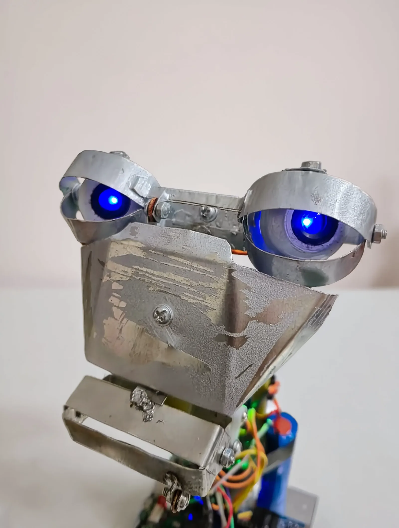 Closeup of the Brutus robot head: sheet-metal face, eyelid rings and glowing blue LED eyes